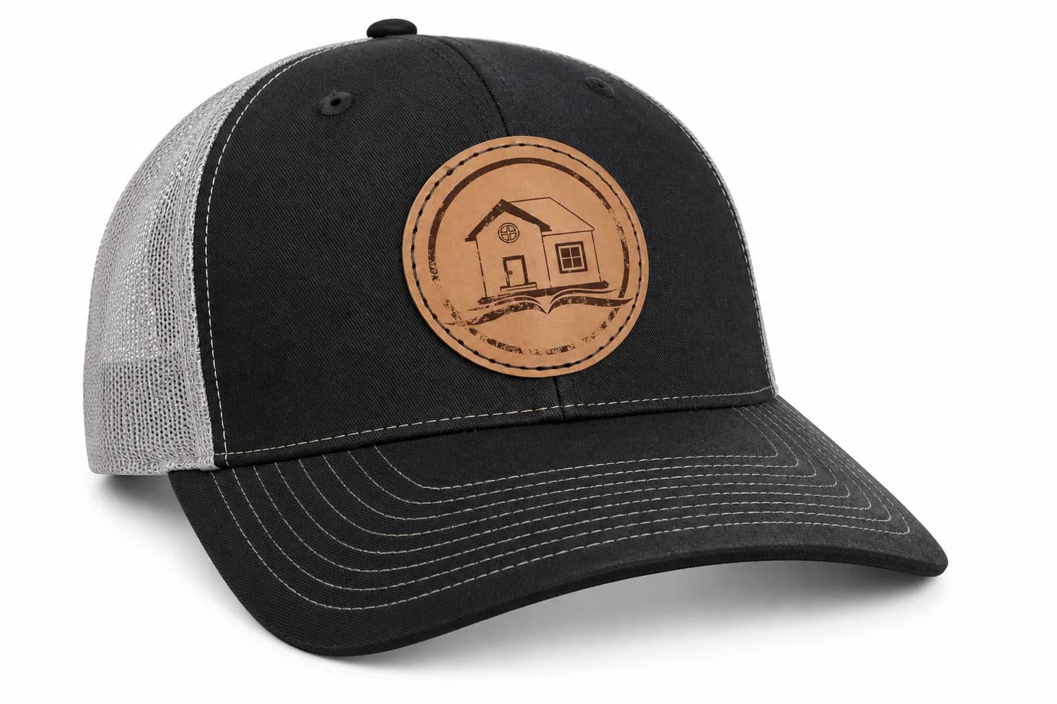 Dark trucker hat with gray mesh, contrasting stitching, and a light tan house-and-book patch.
